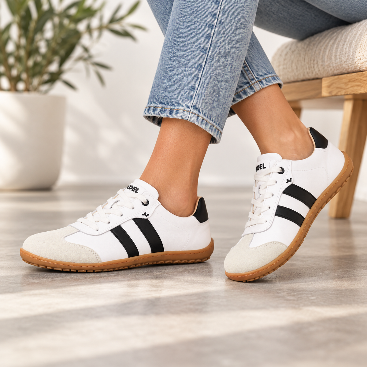 KOEL barefoot sneakers in off-white with black stripes and gum soles, shown close-up on feet.